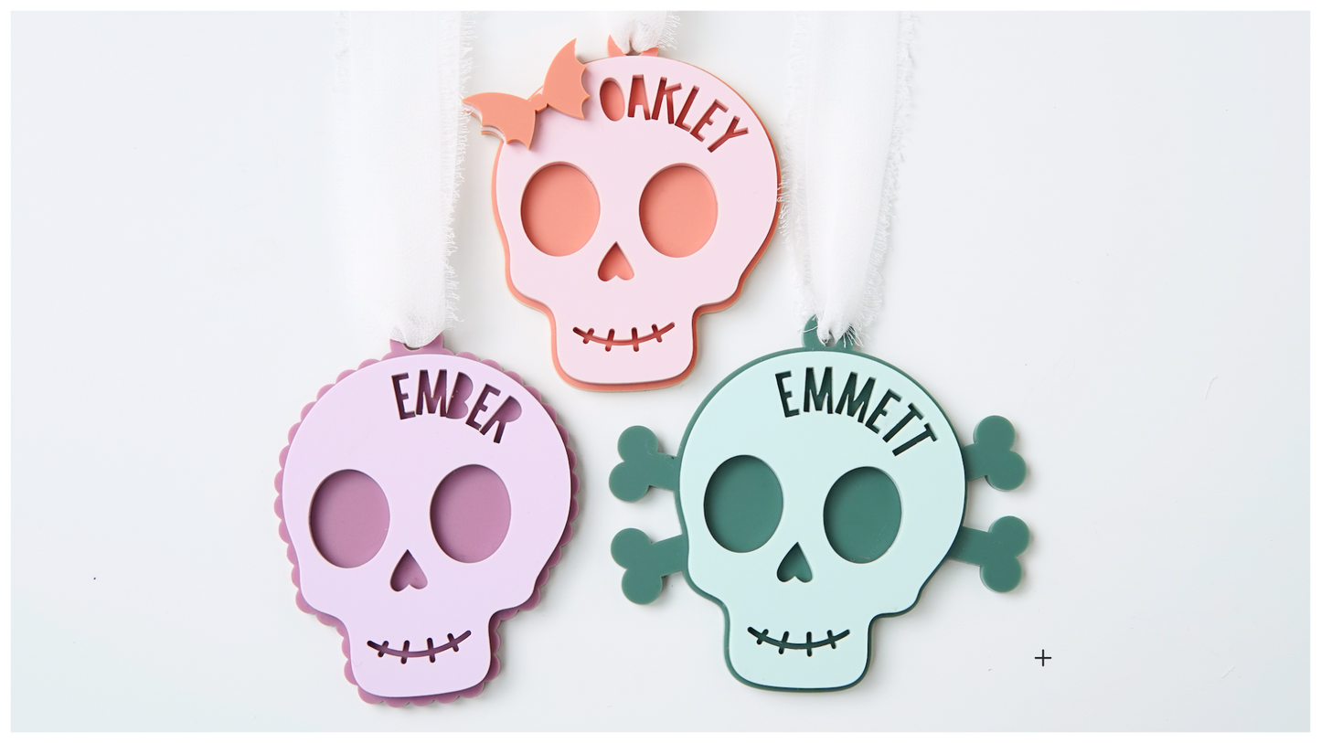 Three colorful skull-shaped acrylic bag tags cutouts with names.