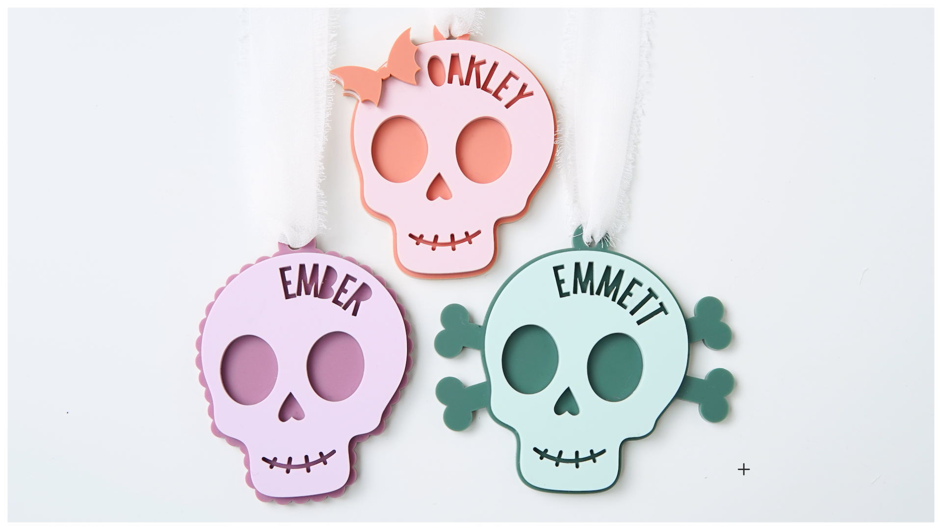 Three colorful skull-shaped acrylic bag tags cutouts with names.